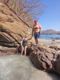 A couple enjoys a sunny day at the beach, exploring rocky shores and shallow waters — a perfect moment for adventure and relaxation.