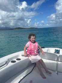 A young girl in a pink life jacket enjoys a sunny day on a boat, showcasing the fun and safety of boating adventures in clear blue waters.