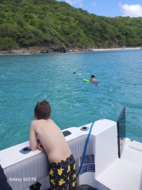 A child watches as another swims with a snorkel in the vibrant turquoise waters, capturing the essence of a fun-filled day on the water.
