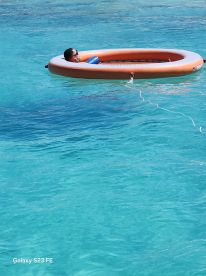 A person relaxes on a floating mat in crystal-clear turquoise waters, perfect for a day of leisure and sun by the sea.
