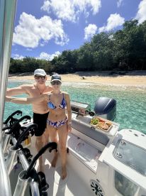 A couple enjoys a sunny day on their boat with a beautiful beach backdrop, featuring a delicious spread of snacks — perfect for a relaxing getaway.