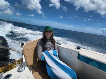 A young woman enjoys a relaxing moment on a boat, wrapped in a towel and smiling against the backdrop of a beautiful ocean view.