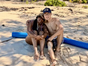 A couple enjoys a relaxing moment on the beach, surrounded by soft sand and greenery — perfect for romantic getaways or beach vacations.