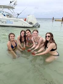 A group of friends joyfully interacts with starfish in shallow waters, showcasing a memorable wildlife experience during their boating adventure.