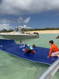 Three kids enjoy a fun day on a water mat while a boat is anchored nearby, capturing the essence of summer adventures at the beach.