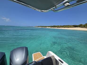 A stunning view from the deck of a boat, showcasing clear turquoise waters and a sandy beach in the distance — perfect for exploring beautiful coastal destinations.