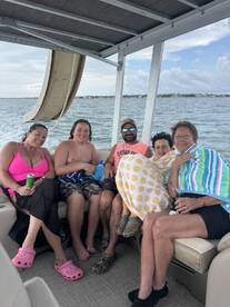 A joyful group of family members relaxes on a boat, enjoying their time together with towels and drinks — perfect for a fun day on the water.