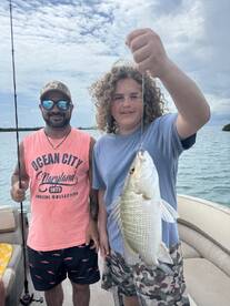 A joyful moment captured as a young boy proudly holds up his catch while fishing with an adult on a boat — a perfect memory of a fun day on the water.