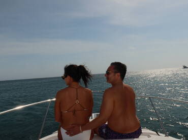 A couple enjoys a romantic moment on the deck of a boat, overlooking the sparkling ocean — perfect for a getaway or special occasion.