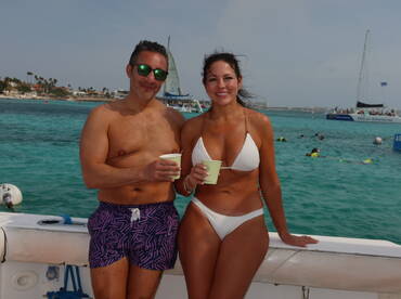 A couple enjoys refreshing drinks while posing on a boat, with a vibrant snorkeling scene in the background — perfect for beachside adventures and romantic getaways.