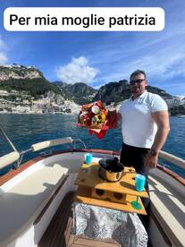 A man surprises his wife with flowers and champagne aboard a boat, creating a romantic atmosphere against a stunning coastal backdrop.
