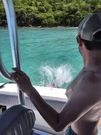 A thrilling moment captured as a person jumps into the crystal-clear waters, creating a splash, while enjoying a day on the boat — perfect for adventure seekers.