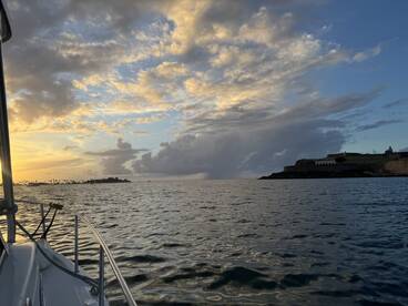 A stunning sunset view from a boat, showcasing a picturesque coastline and island silhouette — perfect for capturing the beauty of a tranquil evening on the water.