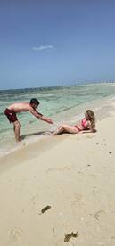 A couple enjoys a playful moment on the beach, with the clear waters and sandy shore creating a perfect backdrop for a romantic getaway.
