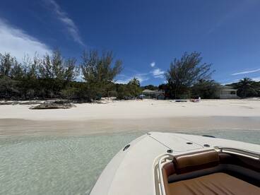 A serene view of a beach with clear waters and lush greenery, featuring the bow of a boat in the foreground — an ideal spot for relaxation and exploration.