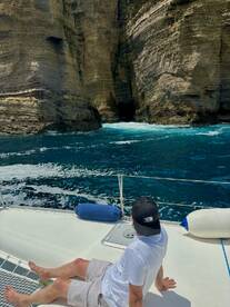 A guest relaxes on the deck of a boat while enjoying stunning views of towering cliffs and turquoise waters, perfect for exploring coastal landscapes.