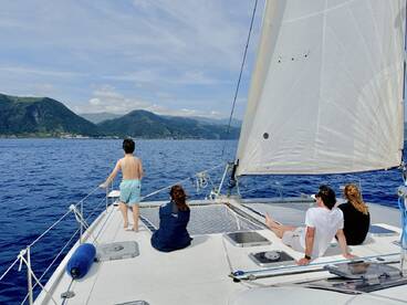 A family enjoys a sailing adventure on a catamaran, with stunning mountain scenery in the background — a perfect day on the water.