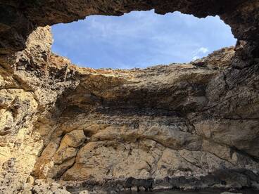 A stunning view of a natural cave formation with a clear blue sky above, showcasing the beauty of coastal landscapes — perfect for adventure seekers exploring hidden gems.