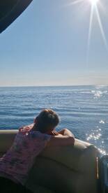 A young person relaxes on the boat, gazing out at the serene ocean under a bright sun — a perfect moment of tranquility on the water.