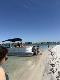 A lively group enjoys a sandbar stop aboard a pontoon boat, with guests relaxing on the shore and in the water — perfect for a fun day out on the water.