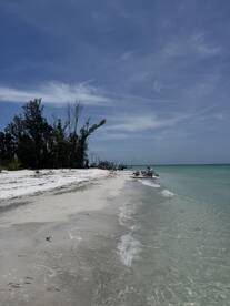 A serene beach scene with a boat anchored near the shore, showcasing the beauty of the coastline and clear waters — perfect for a relaxing day on the water.
