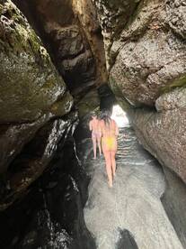 Two friends explore a stunning cave while wading through shallow water, showcasing the beauty of nature and adventure on their trip.