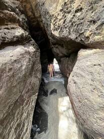A person explores a rocky passageway leading to a sandy beach, showcasing the beauty of natural landscapes and adventure in coastal areas.