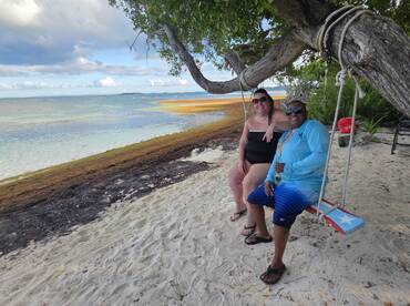 A couple enjoys a relaxing moment on a swing by the beach, surrounded by serene waters and sandy shores — perfect for a laid-back getaway.