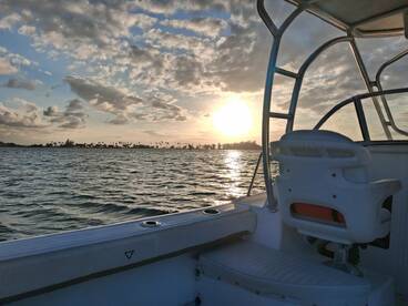 A serene view of a boat at sunset, showcasing the tranquil waters and distant palm trees — perfect for capturing the essence of a peaceful day on the water.