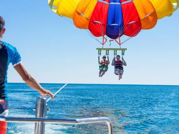 A couple enjoys an exhilarating parasailing adventure over the sparkling ocean, showcasing the thrill of on-water activities.