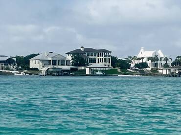 A view of waterfront homes along a shoreline, with turquoise waters in the foreground. The image lacks clarity and detail.