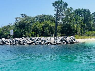 A view of a rocky shoreline with a warning sign, surrounded by clear turquoise waters. The image lacks clarity and detail.