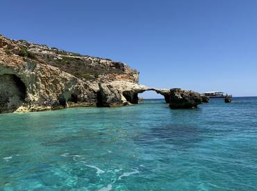 A stunning view of a natural rock formation arching over crystal-clear turquoise waters, showcasing the beauty of the coastline — perfect for scenic boat tours and exploration.