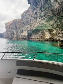A stunning view of rugged cliffs rising above crystal-clear turquoise waters, captured from the deck of a boat — a perfect representation of coastal beauty.