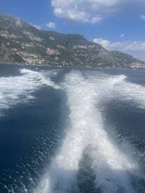 A stunning view of the coastline with a boat's wake cutting through the clear blue waters, showcasing the beauty of the Amalfi Coast.