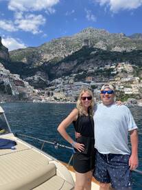 A couple poses on the deck of a boat with stunning coastal scenery in the background, perfect for romantic getaways or scenic tours along the Amalfi Coast.