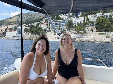 Two friends enjoy a sunny day on a boat, smiling against a picturesque coastal backdrop — perfect for memorable outings and adventures on the water.