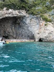 A vibrant scene at a secluded beach with groups of people enjoying the clear waters and exploring the nearby cave — a perfect spot for relaxation and adventure.