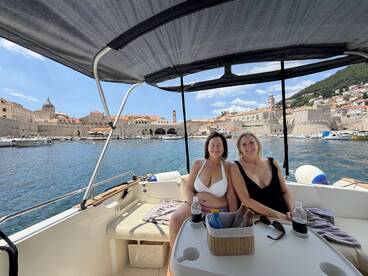 Two friends relax on a boat with drinks, enjoying the scenic view of the historic waterfront — a perfect moment for a summer getaway.