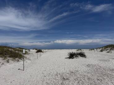 A scenic view of a beach pathway leading to the ocean, framed by sandy dunes and a clear blue sky.