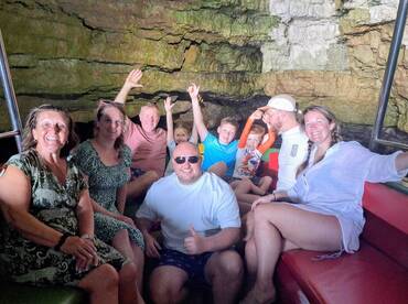 A joyful group of family and friends enjoys their adventure inside a cave, capturing memories together on a boat trip — perfect for family outings and exploration.