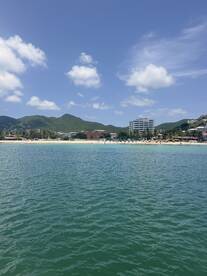 A picturesque view of a beach with clear waters and lush mountains in the background, showcasing a vibrant coastal scene perfect for relaxation and water activities.