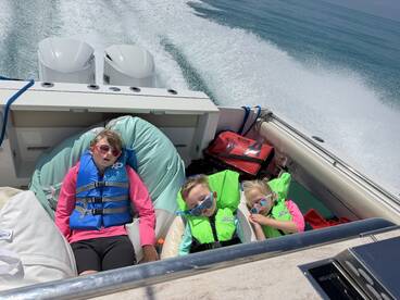 Three children relax on a boat, wearing life jackets and enjoying a sunny day on the water — a perfect moment of fun and safety during their boating adventure.