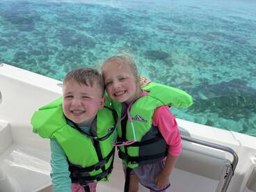 Two children in bright life jackets smile for the camera aboard a boat, with a stunning ocean backdrop — perfect for family adventures on the water.