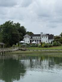 A scenic view of a waterfront house with a dock, surrounded by greenery and cloudy skies, creating a tranquil atmosphere.
