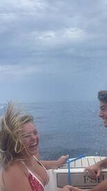 Two friends enjoy a thrilling moment on a boat, laughing and splashing in the water — a perfect snapshot of summer fun on the ocean.