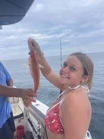 A young woman proudly displays her catch while fishing on a boat, capturing the joy of a successful day on the water.