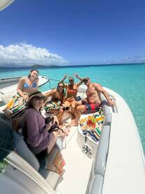 A lively group enjoys a fun day on the water, celebrating with food and drinks aboard their boat, surrounded by stunning turquoise waters.