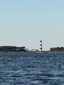 A picturesque view of a black and white lighthouse standing tall against a clear sky, surrounded by tranquil waters — a perfect representation of coastal beauty.