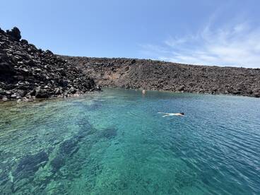 A swimmer enjoys the crystal-clear waters surrounded by a dramatic rocky coastline, showcasing the beauty of a secluded natural swimming spot.